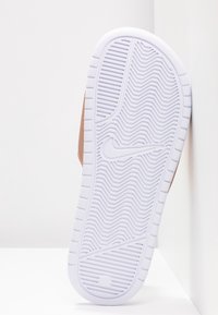 Semelle en caoutchouc blanche d'une basket avec motif ondulé et logo Nike swoosh, inclinée sur un fond blanc d'angle.