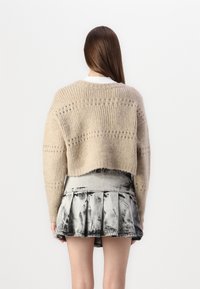 Beige pletený zkrácený svetr s žebrovanou texturou a otevřenými stehny, kombinovaný s vzorovanou černobílou plisovanou sukní.