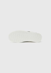 Suola di sneakers bianche con un motivo di presa testurizzato, caratterizzata da una forma liscia e arrotondata e sottili accenti neri lungo i lati.