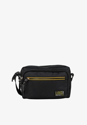 Bolso bandolera de tela negra con dos compartimentos con cremallera, acento amarillo en la cremallera frontal y correa ajustable. Parche con logo en el lateral.