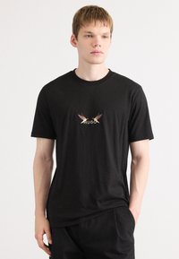 Svart bomulls T-skjorte med grafisk design av to fugler og ordet "HUGO" i gull nederst. Klassisk rund hals og korte ermer.