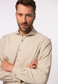 Beige langarmshirt met een gestructureerde stof, met een knoopsluiting bij de kraag en zichtbare knopen aan de voorkant. Aansluitende silhoutte met manchetten.