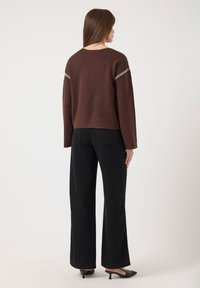 Pull court marron avec des coutures texturées sur les manches, associé à un pantalon large noir taille haute et des escarpins noirs à bout pointu.