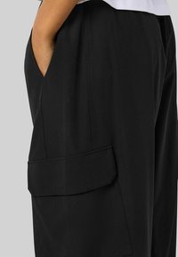 Crne široke hlače napravljene od glatkog materijala, s bočnom džepom s preklopom. Labav kroj i minimalistički dizajn.