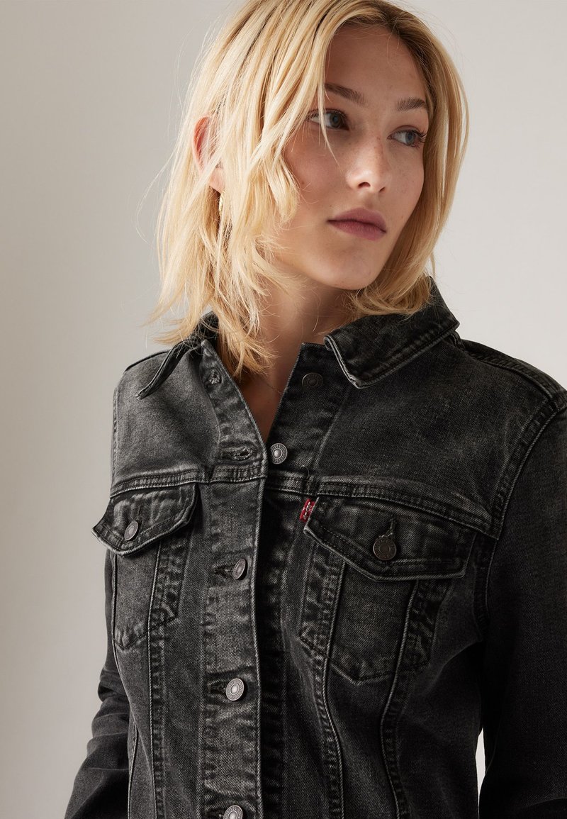 Schwarze Jeansjacke mit durchgehender Knopfleiste, zwei Brusttaschen und klassischem Kragen. Sie hat eine ausgebleichte Textur mit kontrastierenden Knöpfen.