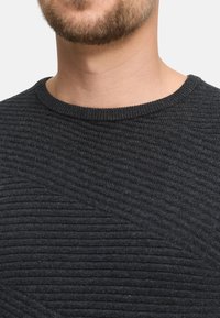 Ciemnoszary sweter o teksturowanym wzorze z prążkami, z wąskim okrągłym dekoltem. Tkanina wydaje się miękka i ciepła, idealna do codziennego noszenia.