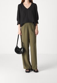 Blusa nera a V con maniche a palloncino, abbinata a pantaloni verdi oliva con vita elastica. Accessoriata con una borsa a spalla nera e sandali chunky.