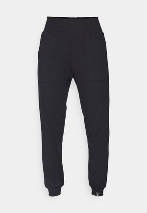 Black jogger pants with a smocked waist, tapered leg, side pockets, and ribbed cuffs. Made of soft, stretchy material.