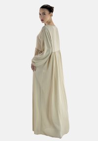 Lange beige jurk met een ronde halslijn, lange mouwen en een losse, vloeiende pasvorm. De stof lijkt zacht met een gladde textuur.