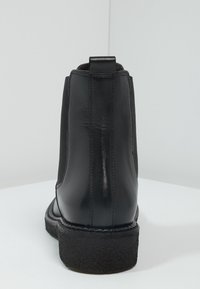 Botín de cuero negro con paneles laterales elásticos, punta redondeada y suela de goma texturizada. Asa en la parte posterior para facilitar el uso. Acabado suave.
