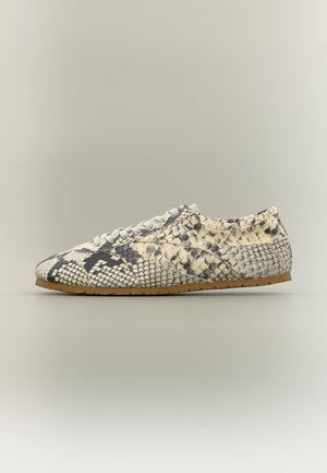 Baskets basses avec motif peau de serpent beige et noir, lacets blancs et semelle marron clair sur fond neutre.