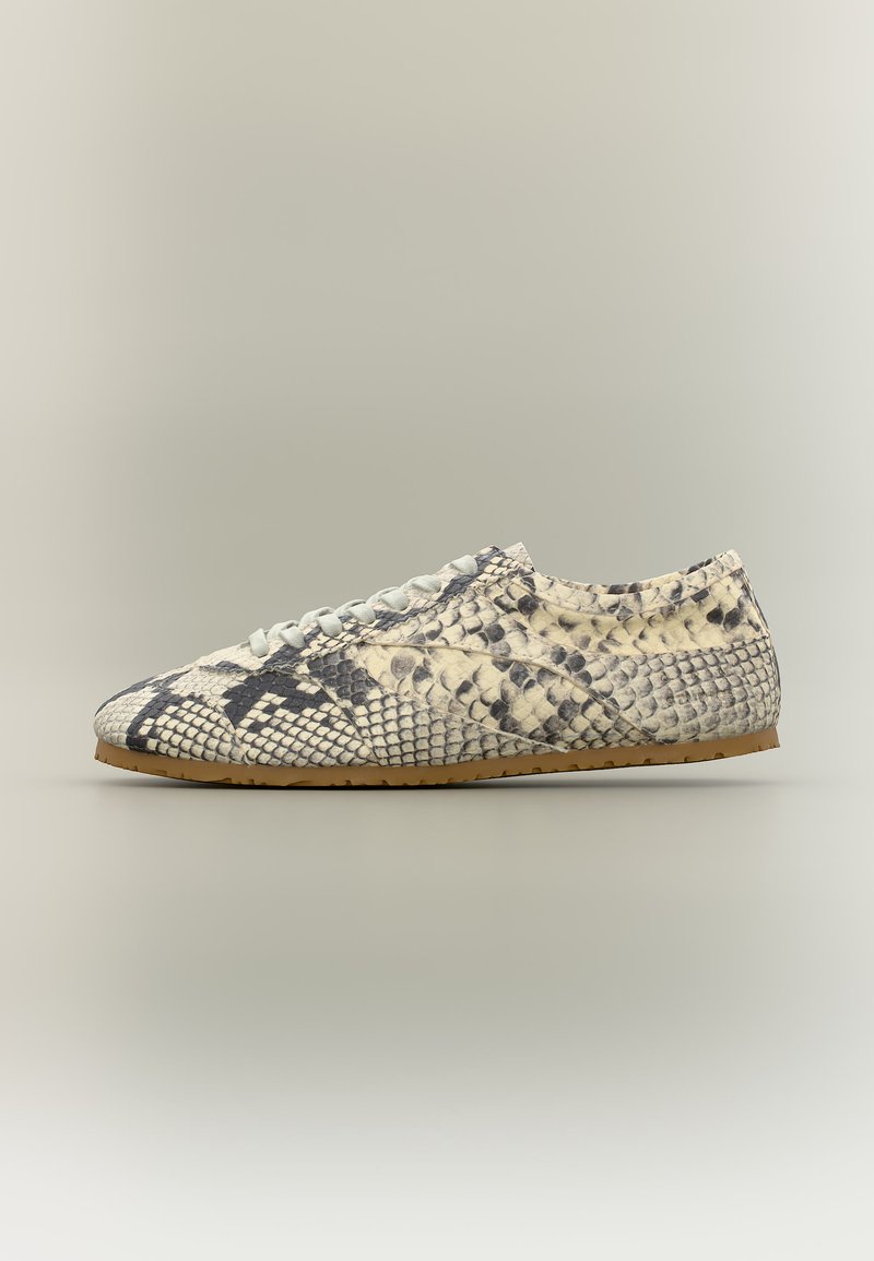 Baskets basses avec motif peau de serpent beige et noir, lacets blancs et semelle marron clair sur fond neutre.