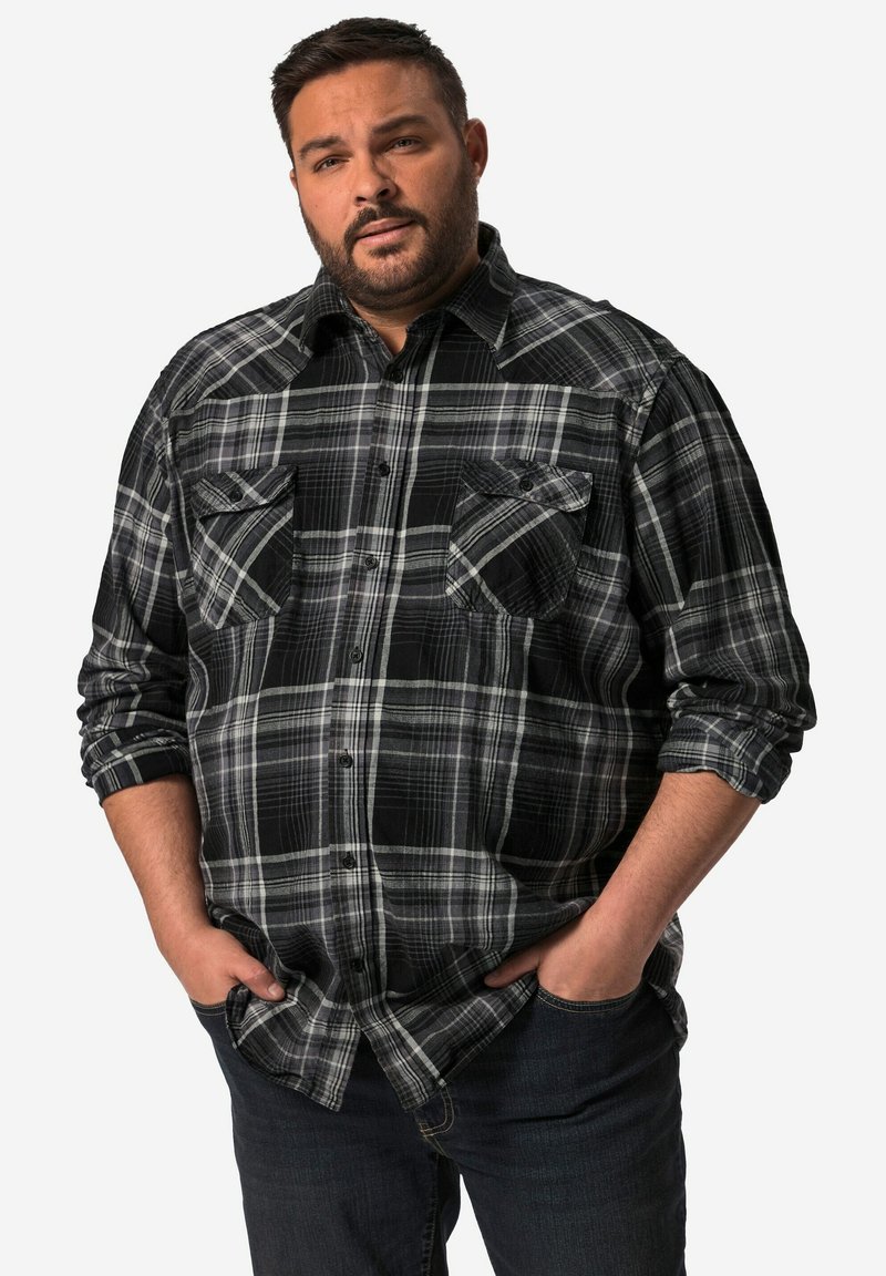 Sort og gråternet flannel-skjorte med knaplukning foran, to brystlommer og opkrøllede ærmer. Båret med mørke jeans.