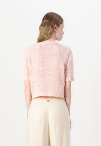 Pull court à manches courtes en tricot rose doux, présentant un motif texturé et un ourlet côtelé. Associé à un pantalon taille haute beige clair.