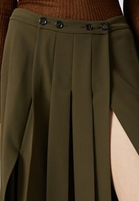 Gonna plissettata verde oliva con due bottoni neri in vita e uno spacco alto fino alla coscia per un tocco di dettaglio e design.