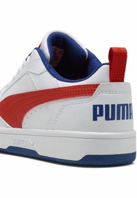 Baskets blanches avec une rayure orange et des accents bleus, en matériaux cuir et textile, semelle plate en caoutchouc, avec le logo "PUMA" sur le talon.