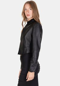 Giacca corta in pelle nera con una texture liscia, caratterizzata da un colletto alto e un design minimalista. Nessuna ferramenta o decorazione visibile.