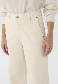 Pantalon large couleur crème en coton avec une texture lisse ; doté d'une fermeture à boutons sur le devant et de poches latérales.