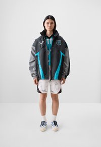 Black and gray zippered jacket with teal accents, paired with white shorts featuring black signatures, and blue and white athletic shoes.