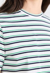 Randig t-shirt med horisontella linjer i marinblått, grönt och vitt. Mjuk bomullsmaterial med rund halsringning och korta ärmar.