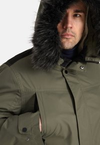 Tamsiai žalia parka striukė su pūsta juoda kapuce, turinti užtrauktuką ir spaudę, taip pat šonines kišenes. Įtraukti tekstūruoti audinio detalės.