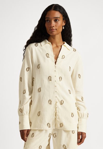 Cremeweißes Hemd mit Knopfleiste und langen Ärmeln, verziert mit gestickten Paisley-Mustern und perlenähnlichen Knöpfen, gefertigt aus einem strukturierten, leichten Stoff.