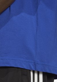 Camiseta de algodón azul con una superficie ligeramente texturizada, con un dobladillo recto, acompañada de pantalones cortos negros que muestran rayas blancas.