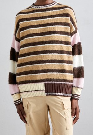 Person iført en stribet sweater i brune, beige, hvide og pink toner, kombineret med beige cargobukser med klaplommer.