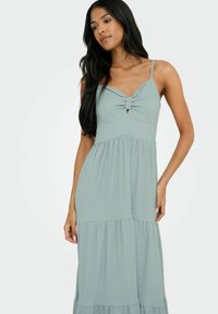 Robe maxi côtelée bleu clair avec des bretelles spaghetti, détail noué à l'avant et ourlet à volants superposés. Tissu doux avec une coupe fluide.