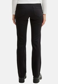 Pantaloni neri a zampa d'elefante con una texture liscia, dotati di due tasche posteriori e una cintura semplice, abbinati a scarpe nere robuste.