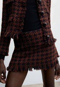 Set di giacca e gonna in tweed intrecciato con motivo a scacchi nero e marrone scuro, caratterizzato da bordi frangiati e bottoni neri lucidi.