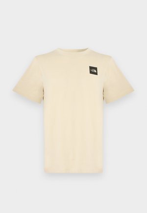 Μπεζ κοντομάνικη βαμβακερή μπλούζα με μικρό μαύρο τετράγωνο λογότυπο στην αριστερή άνω περιοχή του στήθους. Απλός στρογγυλός λαιμός.