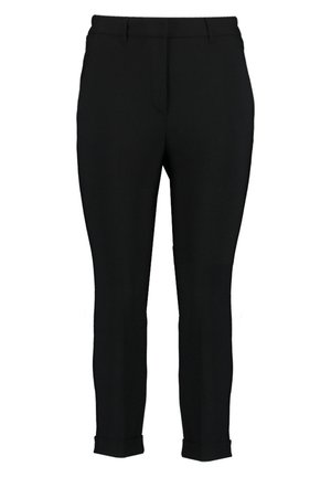 Frau trägt schwarzen maßgeschneiderten Blazer, schwarze verkürzte Hose, metallisch strukturiertes Top mit Schlüssellochausschnitt und schwarze Blockabsatz-Pumps mit Knöchelriemen.