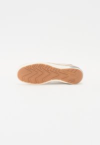 A sneaker talpa textúrált, világosbarna gumiból készült, melyen zigzag minták, krém színű oldalsó akcentusok vannak, és a talpon látható a logó lenyomata.