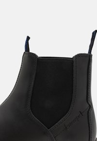 Bota Chelsea negra con un upper de cuero liso, paneles laterales elásticos y una pestaña de tirón texturizada con acentos azul.