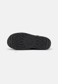 Suela de zapato de goma negra con un patrón de relieve en forma de estrella y acentos circulares. Incluye un logo elevado cerca del talón. Acabado mate.