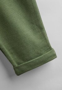 Grøn bomuldsbukseben med en glat tekstur, der har en rullet kant og en ren finish. Ingen synlige mønstre eller hardware-detaljer.