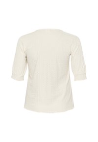 Haut blanc texturé avec un col rond et des manches trois-quarts, présentant un motif subtil et des bords effilochés sur les ourlets des manches.