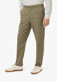 Olijfgroene, lichtgewicht, elastische tailleband broek met zijzakken. Slim fit en een soepele textuur. Gecombineerd met crème sneakers.