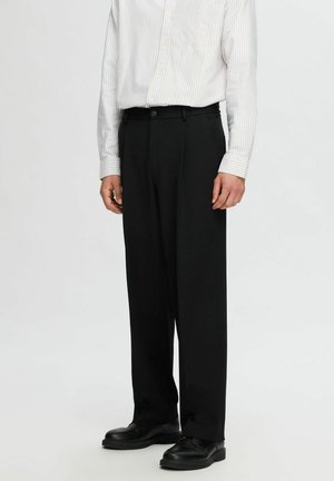Pantalones de pierna ancha negros, fabricados con tejido texturizado, que presentan un pliegue frontal y bolsillos laterales, combinados con una camisa de botones a rayas.