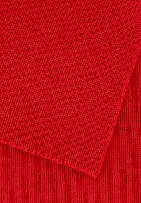 Tissu tricoté rouge montrant un gros plan de la texture côtelée et d'un bord lisse, mettant en avant des coutures fines et régulières tout au long.