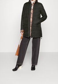 Mörkgrön puffjacka med kviltad textur, hög krage och framfoder. Kombinerad med svarta vida jeans och klackboots. Ingår en brun väska.