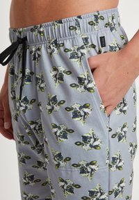 Grijze pyjamashorts met een herhaald patroon van zwarte en groene koeienhoofden, een elastische tailleband met trekkoord en zijzakken.