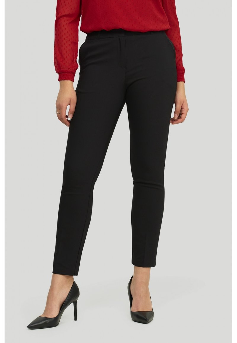 Pantalon noir sur mesure, coupe slim, confectionné dans un tissu lisse, doté de poches avant et d'un devant plat. Associé à des escarpins pointus.