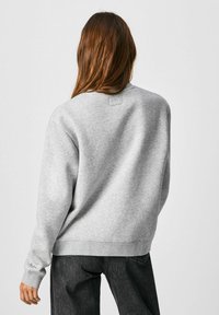 Sudadera gris de corte holgado, con puños acanalados y cuello redondo. Textura suave y diseño minimalista sin patrones ni detalles visibles.