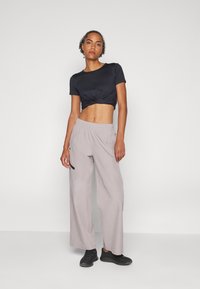 T-shirt nera a braccio corto e taglio cropped, abbinata a pantaloni ampi grigi chiari con vita elastica e sneaker nere.