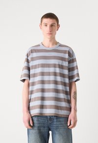 Striped t-shirt i lyseblå og brun. Blødt bomuldsstof, afslappet pasform, med rund halsudskæring og korte ærmer. Logo detaljer på brystet.
