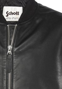 Schwarze Leder-Bomberjacke mit einem Reißverschluss vorne, geripptem Kragen und strukturierter Oberfläche, die ein auffälliges Markenlabel im Inneren hat.