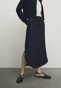 Tummansininen midi-hame, jossa on sivuaukot, valmistettu sileästä kankaasta, yhdistettynä kevyeseen mustaan neuleeseen ja mustiin tasapohjaisiin kenkiin.