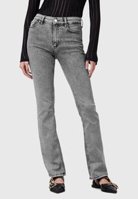 Jeans grigi alti in vita con vestibilità dritta, caratterizzati da cuciture visibili e design a cinque tasche, abbinati a scarpe basse nere.